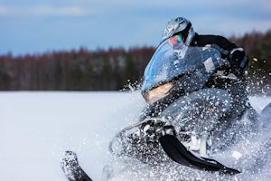 A snowmobile rider snow drifting on a sunny day.