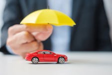 Businessman hand holding a yellow umbrella that's covering a red car toy on a table.