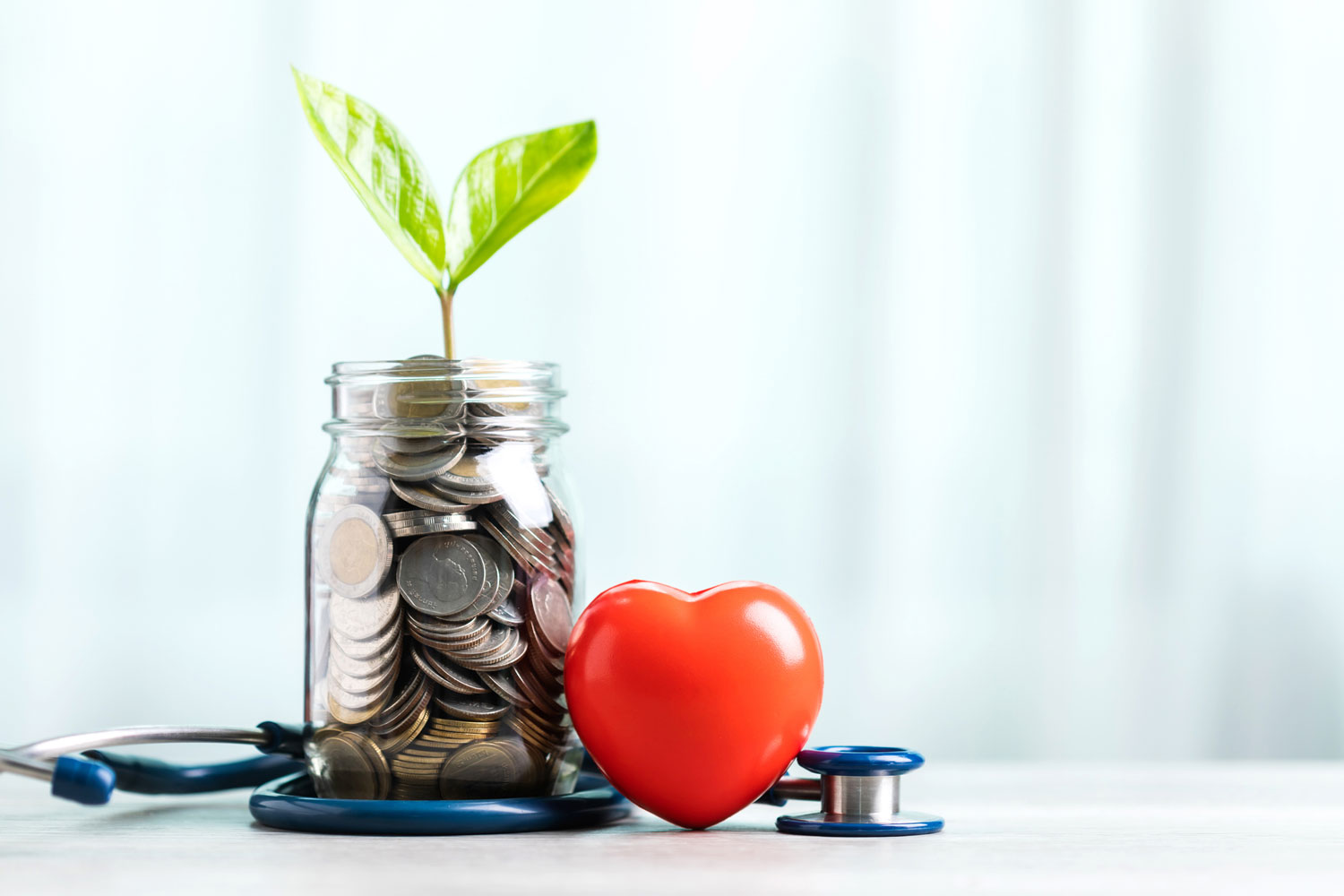 A jar filled with coins and a small plant in the center, accompanied by a heart and a stethoscope.