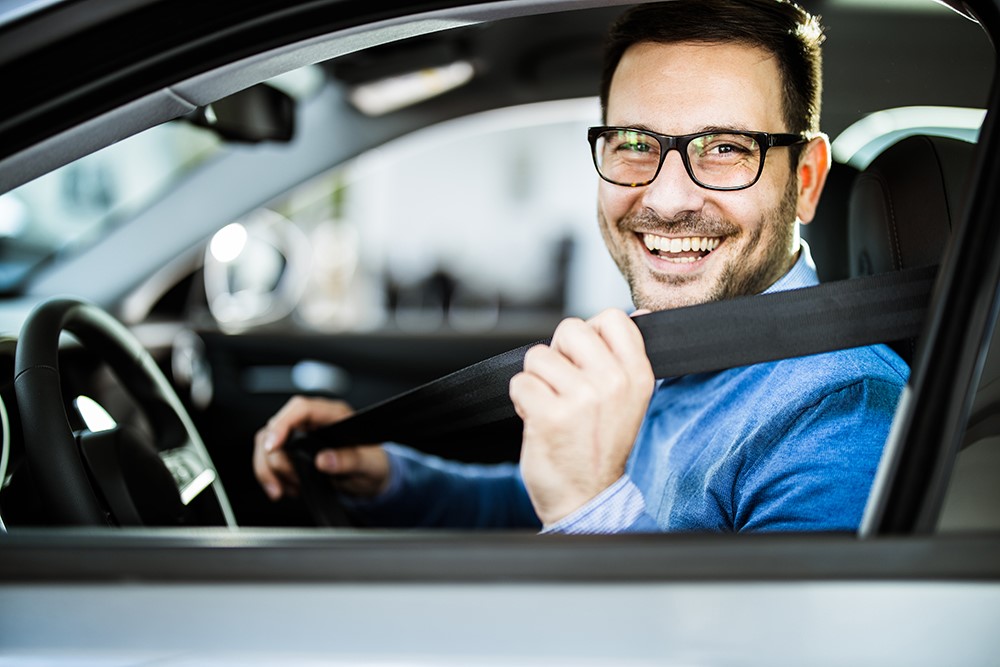 A person sitting in a car seat, smiling and appearing happy.