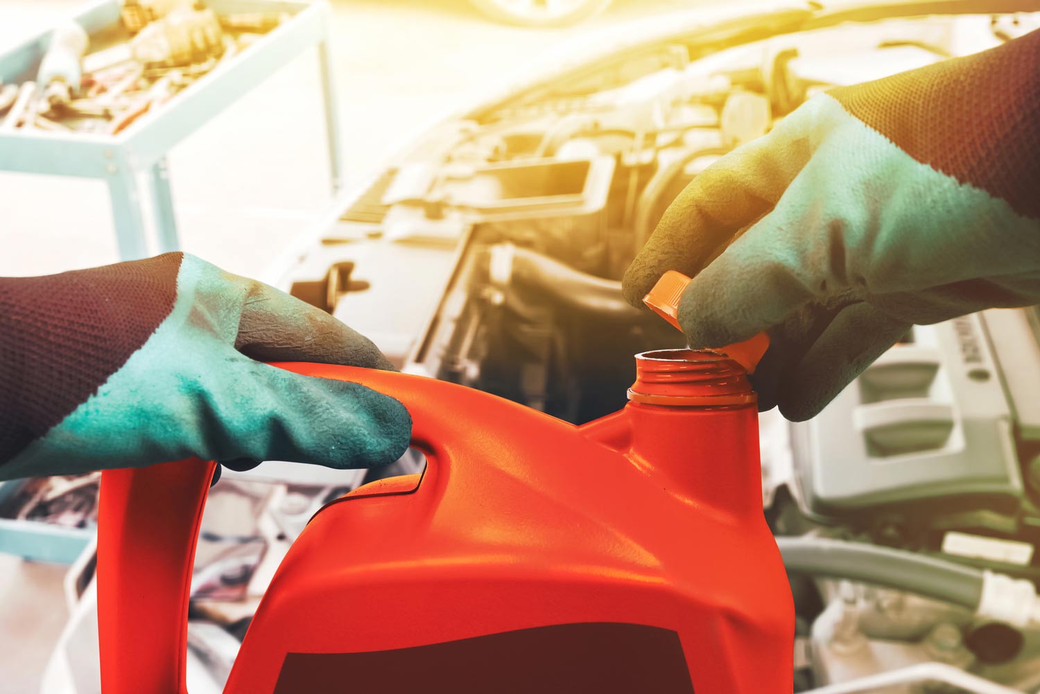 Mechanic opens the cap of a red colored gallon of motor oil.