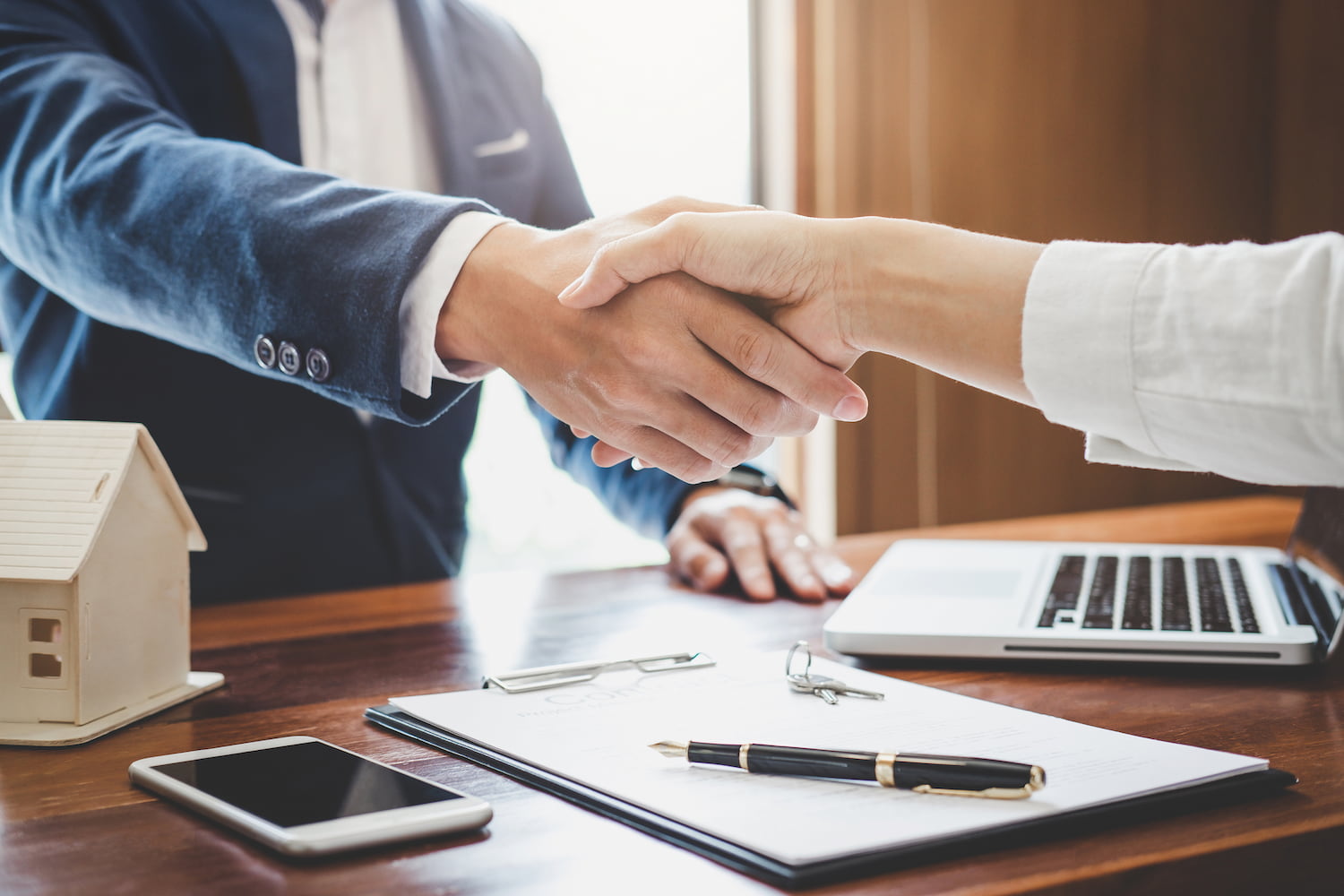 Two people shaking hands across a table with documents on it.