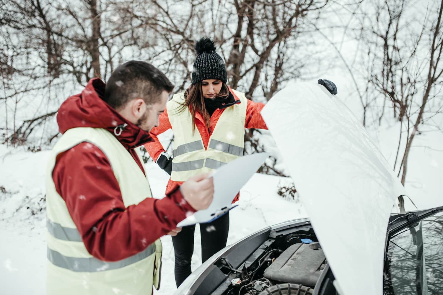 Two people in winter conditions, troubleshooting a car with the hood raised.