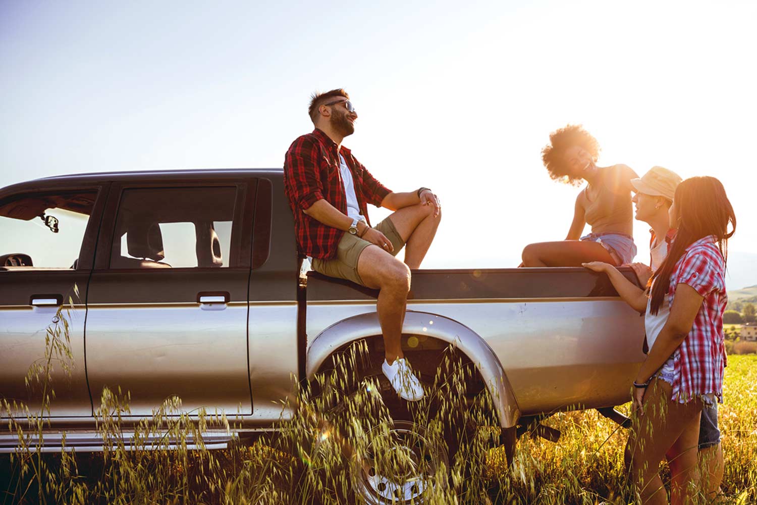 Friends having a chat while setting on a truck in an open field on a sunny day