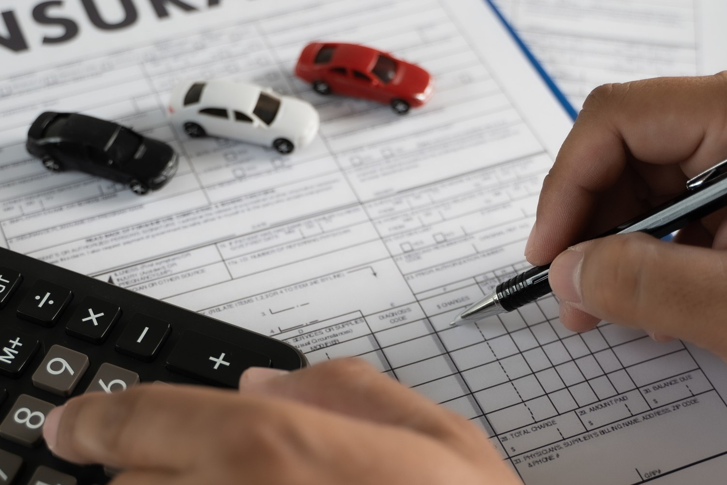 3 cars lined up on form, a person is writing with a pen in one hand and calculator in the other.